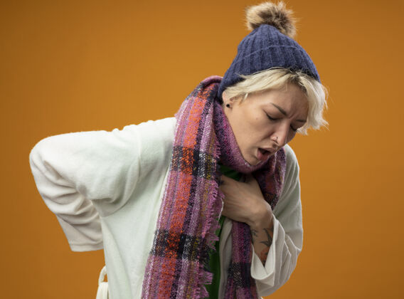 咳嗽生病的不健康的女人 短发 戴着暖和的围巾 戴着帽子 站在橙色的背景上感觉不舒服 咳嗽 感冒生病暖和头发