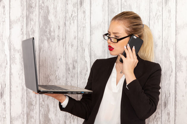 工作正面图穿着黑色夹克的年轻女商人在白色的表面上用笔记本电脑和电话交谈谈话商务女性夹克
