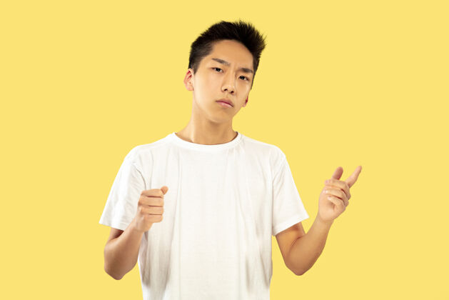 成功黄色摄影棚背景上的韩国年轻人半身像穿白衬衫的男模手握和邀请人类情感的概念 面部表情正面视图流行的颜色事业男士手势