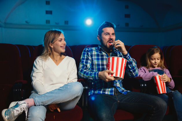观众年轻的白种人家庭在电影院 房子或电影院看电影看起来富有表现力 惊讶和情绪化独自坐着玩关系 爱情 家庭 童年 周末时间看成人男