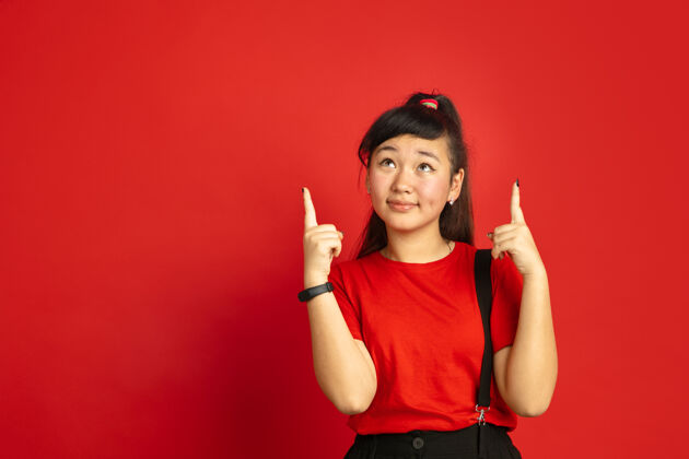 公司亚洲青少年的肖像画被隔离在红色工作室的背景上美丽的深褐色女性模特 留着随意的长发人类情感的概念 面部表情 销售 广告指向上亚洲人帅职业