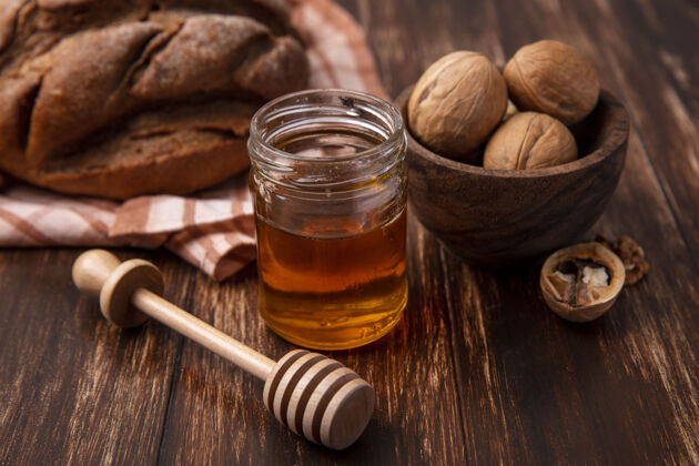 核桃前视图蜂蜜在一个罐子里 核桃和一条黑面包放在木制背景上面包天然面包