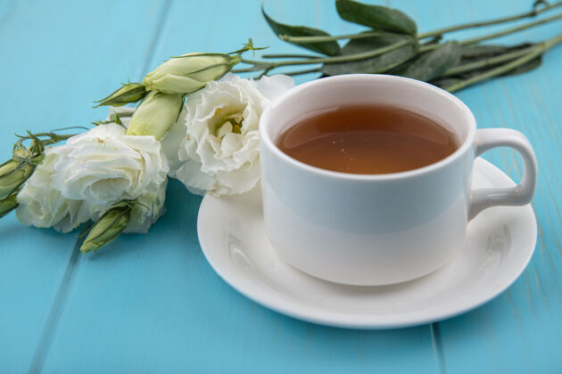 桌子茶碟上的茶杯和蓝色背景上的花的侧视图杯子饮料景观
