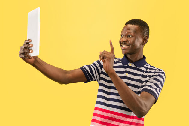 非洲快乐的非洲裔美籍年轻男子 以平板电脑隔离在黄色工作室背景下 面部表情美丽的男性半身肖像人类情感的概念 面部表情欢呼微笑商人