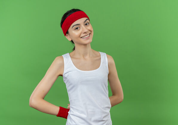 姿势身穿运动服的年轻健身女 头戴花环 快乐而积极地微笑着站在绿色的墙上快乐健康人