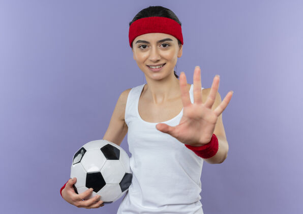 停身穿运动服的年轻健身女 头戴足球带 手掌张开 站在紫色的墙上做停车标志市民球姿势