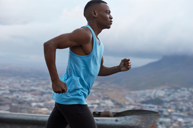 运动运动型深色皮肤跑步者穿蓝色马甲 参加铁人三项比赛 有健身生活方式 模特对着模糊的户外岩石风景 在快速运动中拍照户外动机景观