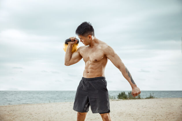 年轻年轻健康的男子运动员在海滩上做深蹲交叉身体沙滩