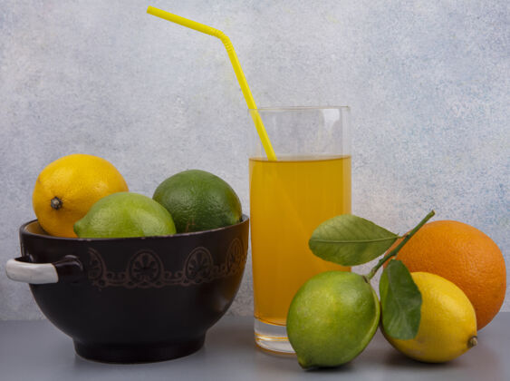 柠檬前视图柠檬与酸橙在平底锅与一杯橙汁的灰色背景新鲜柑橘酸橙