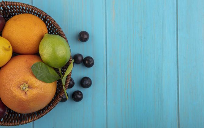 顶部顶视图复制空间水果混合在一篮子葡萄柚橘子柠檬柠檬和樱桃李子在一个绿松石背景复制绿松石李子