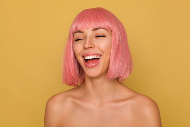 鲍勃可爱的年轻粉红头发的女性 留着时髦的短发 闭着眼睛 站在芥末墙上欢笑前锁肖像高兴