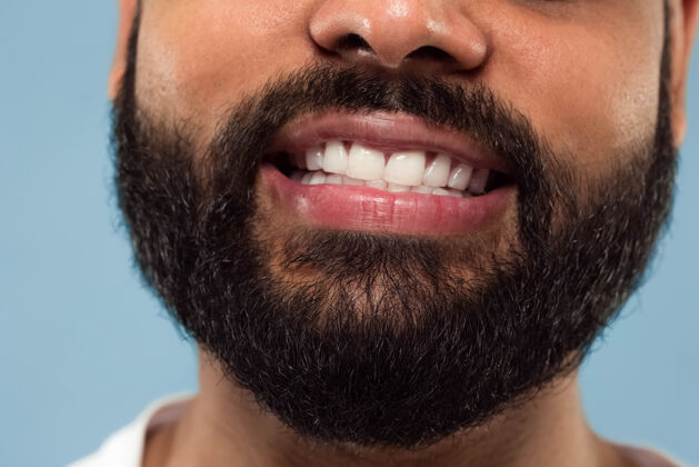 微笑年轻的印地安人的脸的特写肖像 胡子 白色的牙齿和蓝色背景上的嘴唇微笑人类的情感 面部表情 广告概念负面空间就业企业家公司