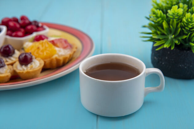 木制一杯茶的侧视图 蓝色木制背景上有一盘馅饼饮料桌子馅饼