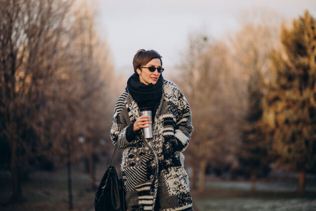 温暖的衣服早上喝咖啡在公园散步的年轻女子服装街头风格黎明