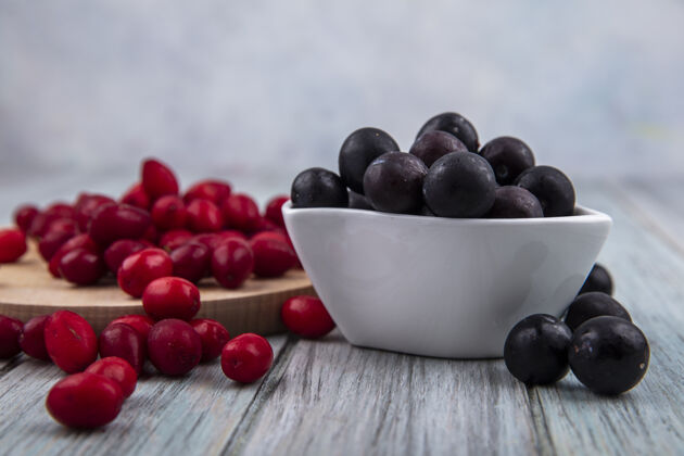 皮肤侧视图黑皮肤黑刺上一个白色的碗与红色的山茱萸浆果隔离在一个木制厨房板上的灰色木制背景山茱萸壁板季节