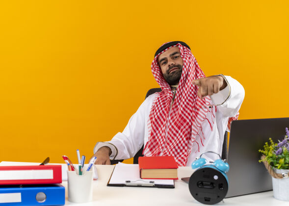 穿身着传统服装的阿拉伯商人坐在桌子旁用手指着办公室工作商务人士工作手指