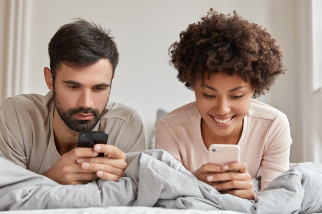 小工具不同种族的吸毒男女合影 在床上使用手机 连接无线网络 享受周末的早晨 有欢快的表情现代科技理念年轻人不刮胡子男人
