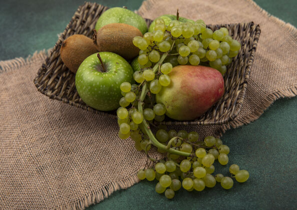 水果侧视图绿色背景上的米色餐巾上的一个立场上的葡萄 猕猴桃和梨绿色苹果绿色新鲜米色