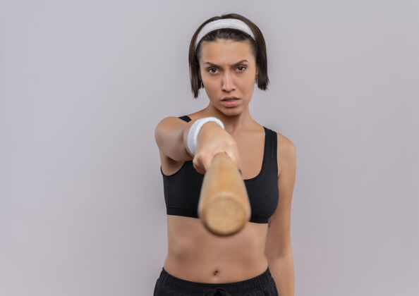 脸穿着运动服的年轻健身女 正脸站在白墙上 用棒球棒指着摄像机姿势运动装站