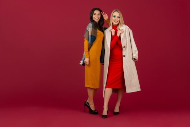 金发两位穿着秋冬时装礼服和外套的时尚女性在红墙上孤零零地摆着姿势女人女性魅力