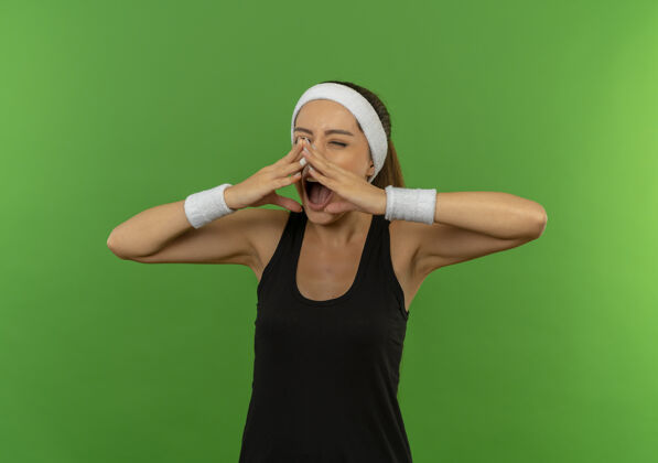姿势身穿运动服的年轻健身女 戴着头巾 手举在嘴边 站在绿色的墙壁上兴奋地喊着喊叫女兴奋