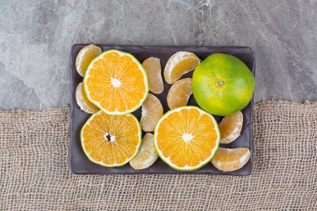 粗麻布一堆橘子和一段一段的放在黑盘子里新鲜切片柑橘