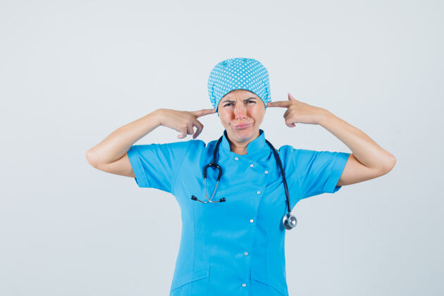支架女医生用手指塞住耳朵 穿着蓝色制服 看起来很恼火正视图实验室工作人员疾病