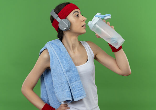 市民穿着运动服的年轻健身女 头上戴着头巾 肩上扛着一瓶水 站在绿色的墙上 准备运动后喝人运动服头带