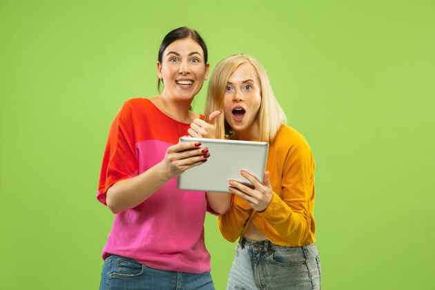 女性在绿色工作室背景上 穿着休闲服装的漂亮迷人女孩的肖像女朋友或女同性恋者使用平板电脑取乐或付款lgbt的概念 人类情感 爱情 关系关系微笑Lgbt