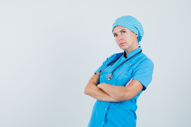 病人身穿蓝色制服的女医生交叉双臂站在那里 面带沉思 俯视前方肖像女人外科医生