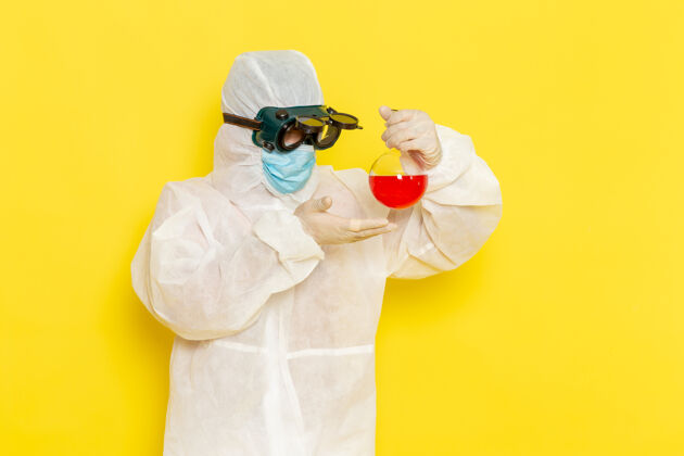 科学正面图穿着特殊防护服的男科学工作者在黄色的桌子上拿着装有红色溶液的烧瓶解决方案套装工人