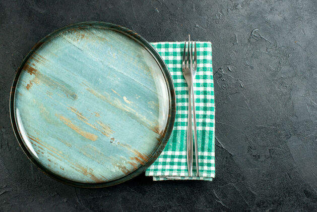 刀顶视图圆形餐盘餐刀和餐叉上绿色和白色方格餐巾上黑色表面自由空间顶部餐巾玻璃