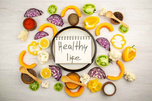 顶部俯瞰健活写在笔记本上的圆板上切菜不同的调料放在白色的小碗面上香料五颜六色蔬菜