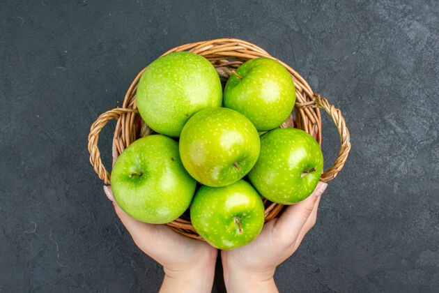 酸橙俯视新鲜的苹果在柳条篮子在黑暗的表面在女性手新鲜苹果多汁维生素