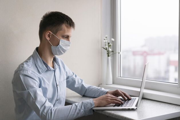 大流行戴着医用面罩的人在智能手机上工作的侧视图笔记本电脑流行病病毒