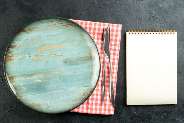 圆盘子俯视图圆形餐盘餐刀和餐叉放在红白餐巾上黑桌上的记事本上晚餐刀叉子