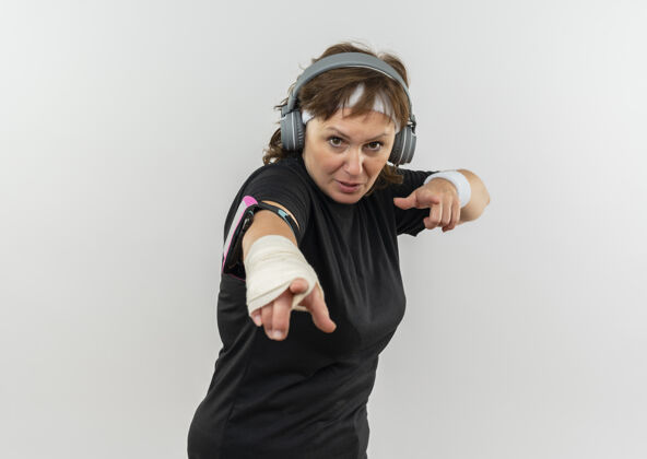 女士中年运动女性 身穿黑色t恤 头戴头带 头戴耳机 食指指向白色墙壁站着手指目录