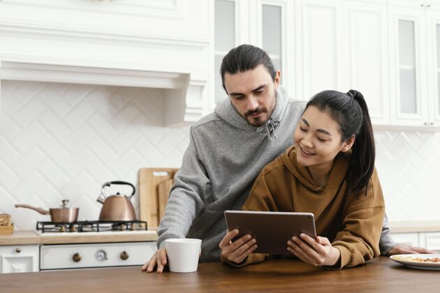 成人一对夫妇在厨房吃早餐 并使用平板电脑休闲时间室内科技
