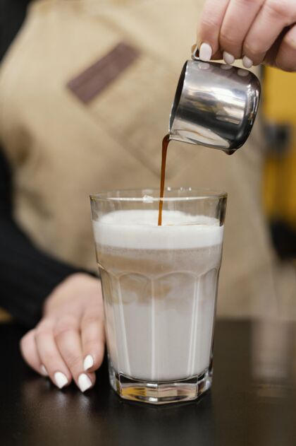 专业女咖啡师在牛奶杯里倒咖啡的正面图职业垂直咖啡店