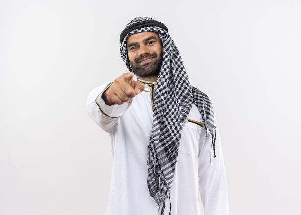 手指身着传统服装的阿拉伯男子微笑着用手指着白墙站着指着传统
