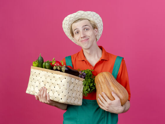 帽子年轻的园丁穿着连体衣戴着帽子拿着装满蔬菜的箱子抱着微笑脸