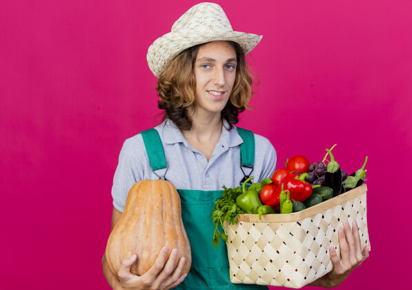 新鲜年轻的园丁穿着连体衣戴着帽子拿着装满新鲜蔬菜的箱子园丁帽子抱着