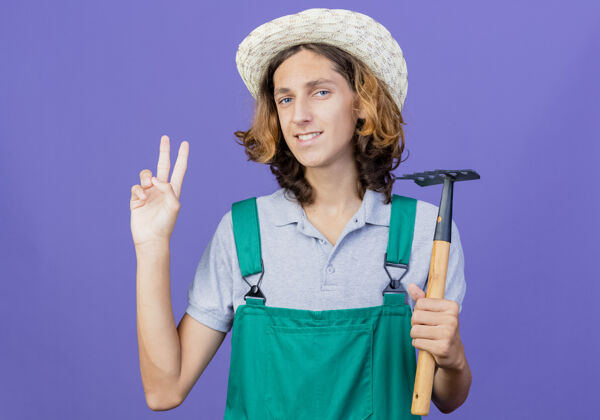 表演年轻的园丁穿着连体衣戴着帽子拿着迷你耙子穿年轻连身衣