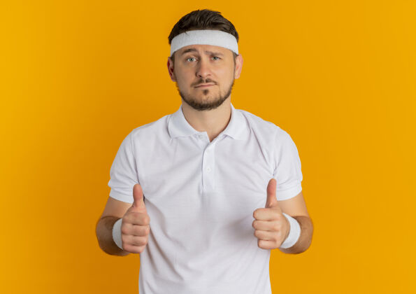 年轻身穿白衬衫 头箍竖起大拇指 站在橙色墙壁上望着前方的年轻健身男子男性小伙子看