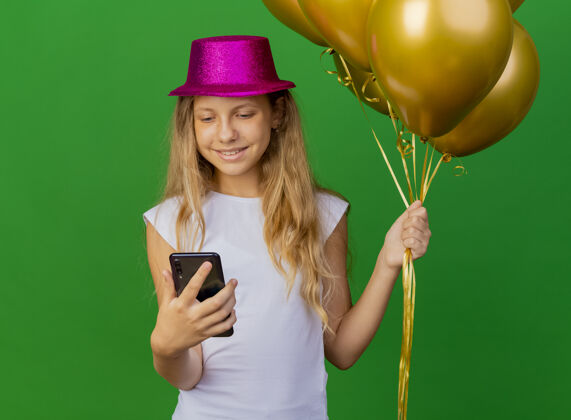 节日戴着节日帽子拿着智能手机的漂亮小女孩站着女孩快乐