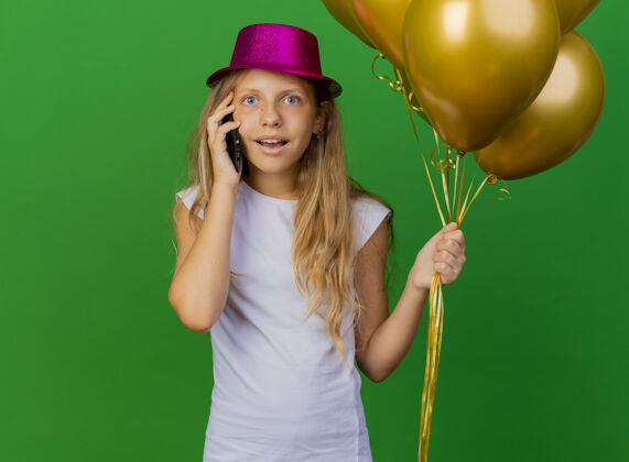 站戴着节日帽子拿着智能手机的漂亮小女孩派对快乐生日