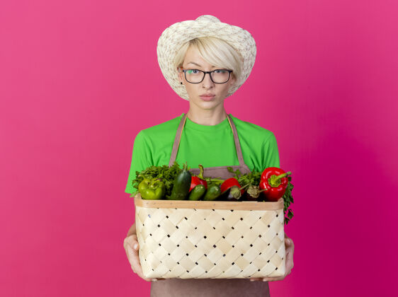 围裙一位年轻的园丁 围着围裙 戴着帽子 手里拿着装满蔬菜的箱子年轻花园女人