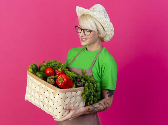 女人一位年轻的园丁 围着围裙 戴着帽子 手里拿着装满蔬菜的箱子满满的年轻人帽子