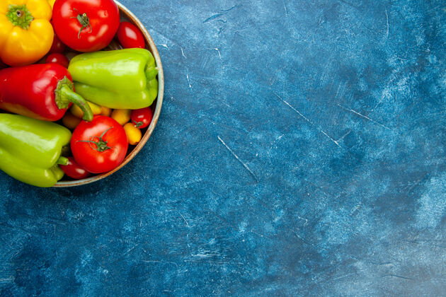 顶部上半视图蔬菜樱桃西红柿不同颜色甜椒西红柿在蓝色桌子上的碗与自由的地方蔬菜胡椒碗