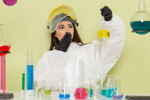 化学正面图：穿着特殊防护服的女化学家在绿色表面上拿着黄色溶液防护保持实验室外套